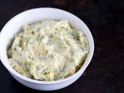 Creamy room temperature herbed compound butter in a white bowl on a dark background.
