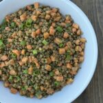Lentils and small diced papaya with fresh herbs in a large white bowl on a wood background.