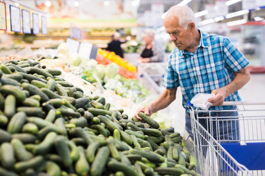 An image of an elderly man shopping for cucumbers in the grocery store.