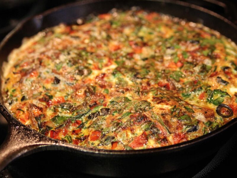 Close up of Bacon, Onion, and Olive Frittata in a cast iron pan.