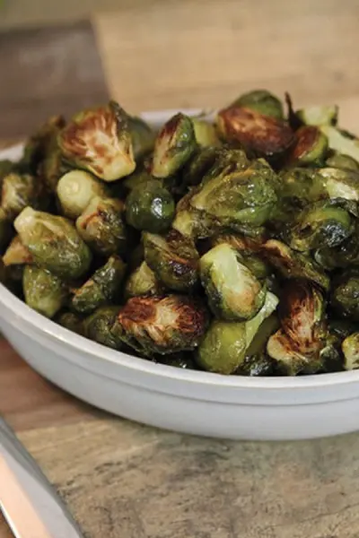 Close up of roasted Brussels sproutps in a white dish on a wood table/