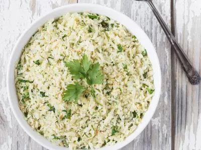 Wide image of Lemon Parsley Cauliflower "Rice" in a white bowl with a white and gray distressed wood background.