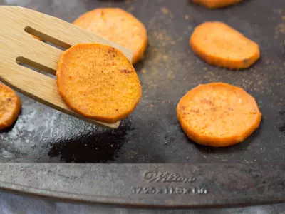 Baked Spiced Sweet Potato (circle cut) on a seasoned baking sheet with potato lifted on wooden spatula.