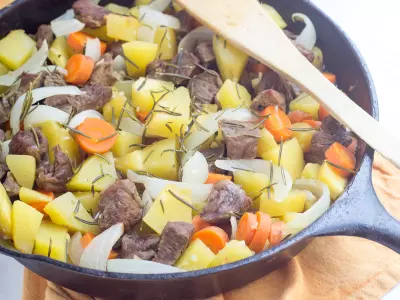 Horizontal image of pressure cooker lamb stew with acorn squash, carrots, and onions presented in a cast iron pan.