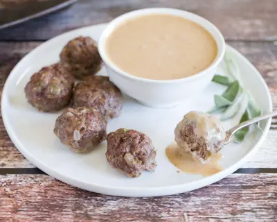 Asian meatballs on white plate with dipping sauce in white bowl.