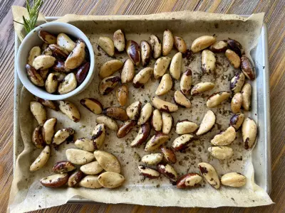 Roasted Brazil Nuts on a parchment -ined sheet pan with some in a small white bowl.
