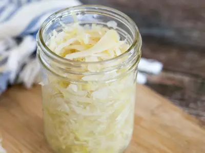 Sauerkraut in a small glass jar on a light wood counter.
