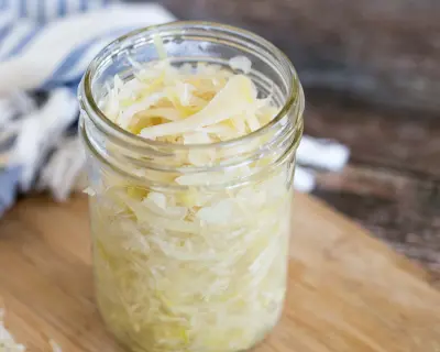Sauerkraut in a small glass jar on a light wood counter.