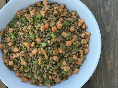 Lentils and small diced papaya with fresh herbs in a large white bowl on a wood background.