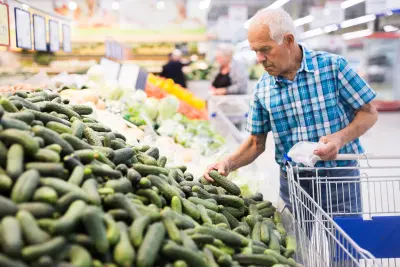 An image of an elderly man shopping for cucumbers in the grocery store.